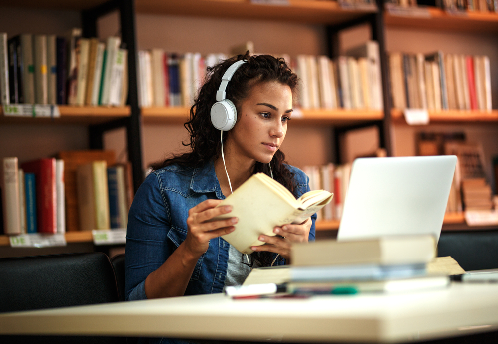 young woman in library listening to music wearing white headphones