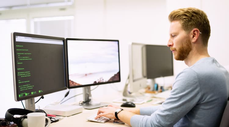 male programmer working on computer with two screens