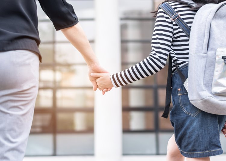 mother holding hands with daughter to school