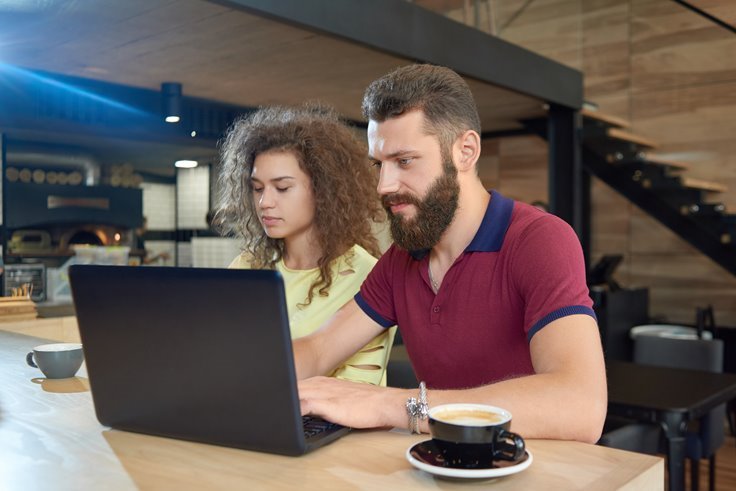 man and woman working together on laptop at cafe